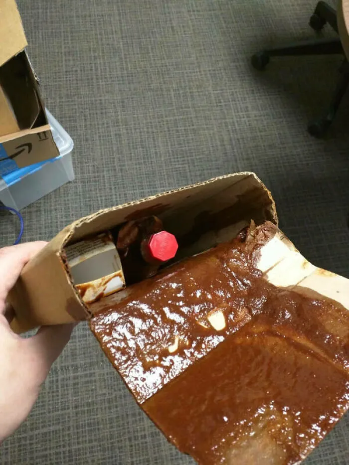 Caja de cartón rota y manchada por derrame de salsa, descuido de repartidores.