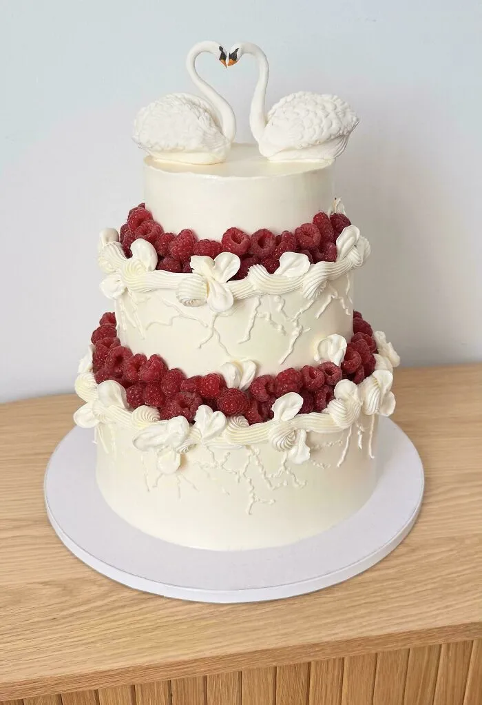 Pastel elegante de bodas decorado con frambuesas frescas y cisnes de repostería.