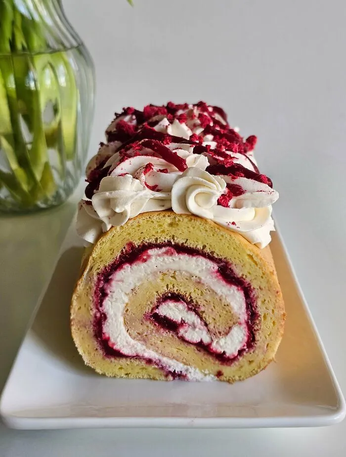 Brazo de reina o rollo de masa relleno de crema y frutos rojos, arte en repostería.